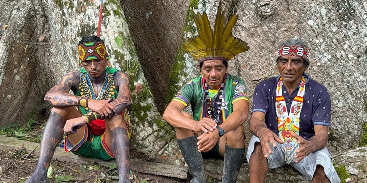 Três homens indígenas sentados junto a uma árvore
