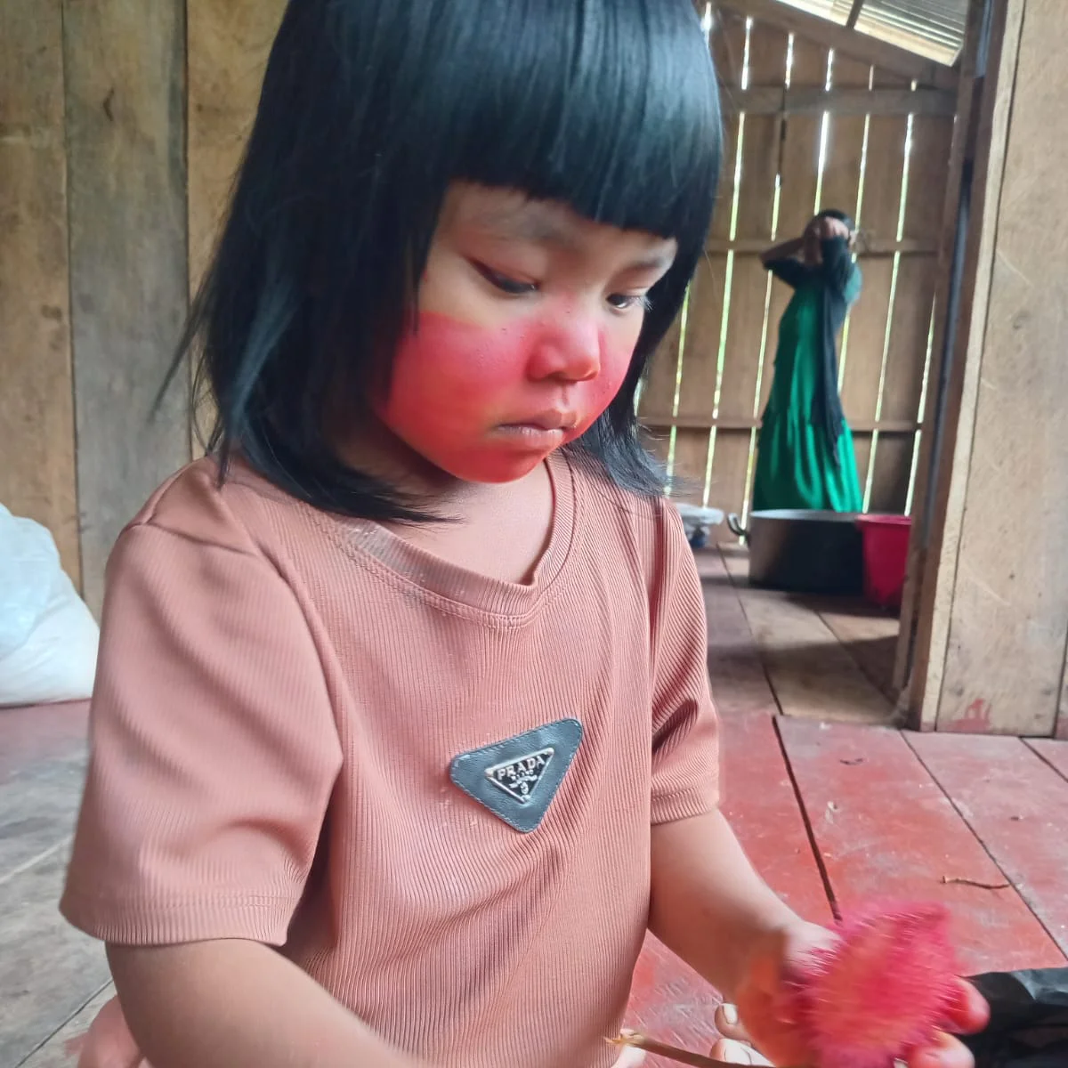 Criança com pintura facial vermelha observando um objeto vermelho dentro de casa